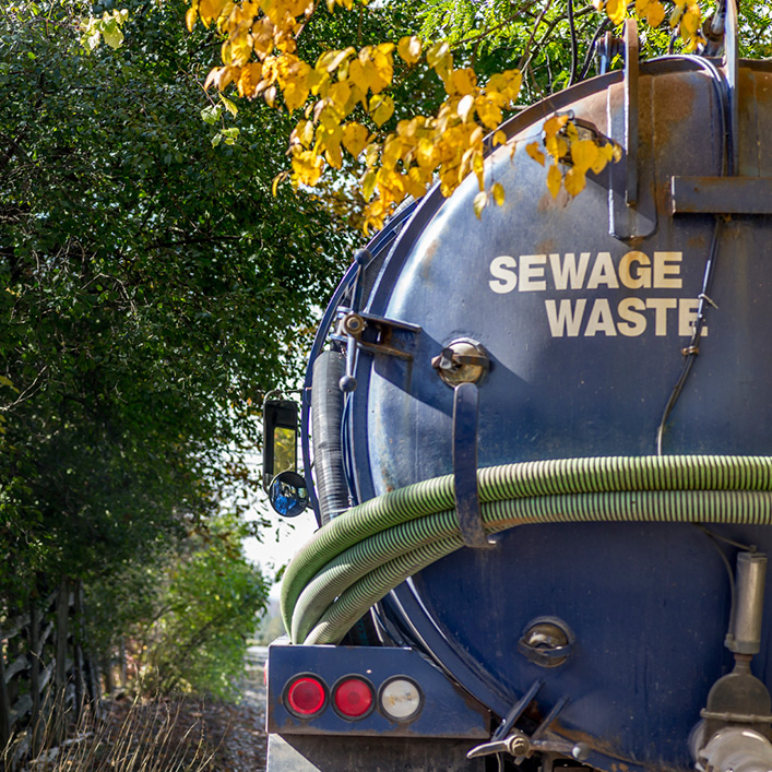 A blue sewage waste truck driving down a road